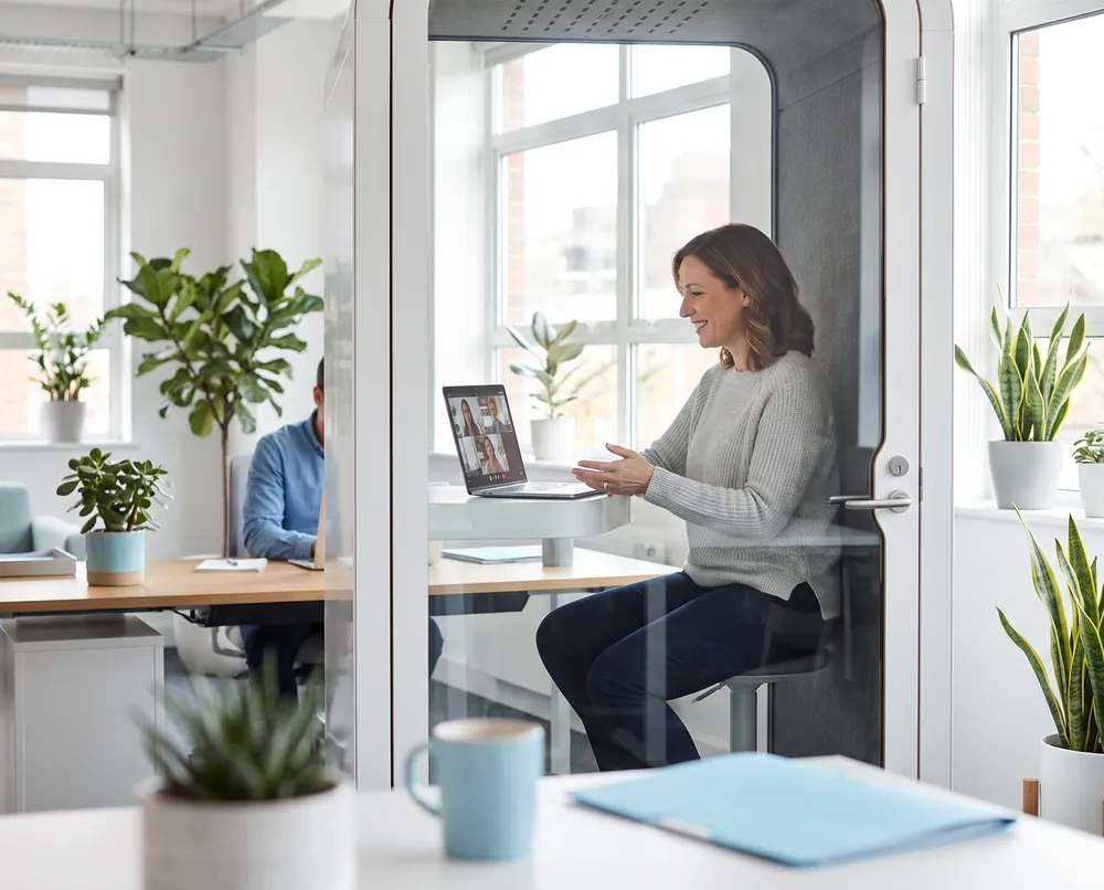 Employee in an office phone booth during a video consultation on a laptop